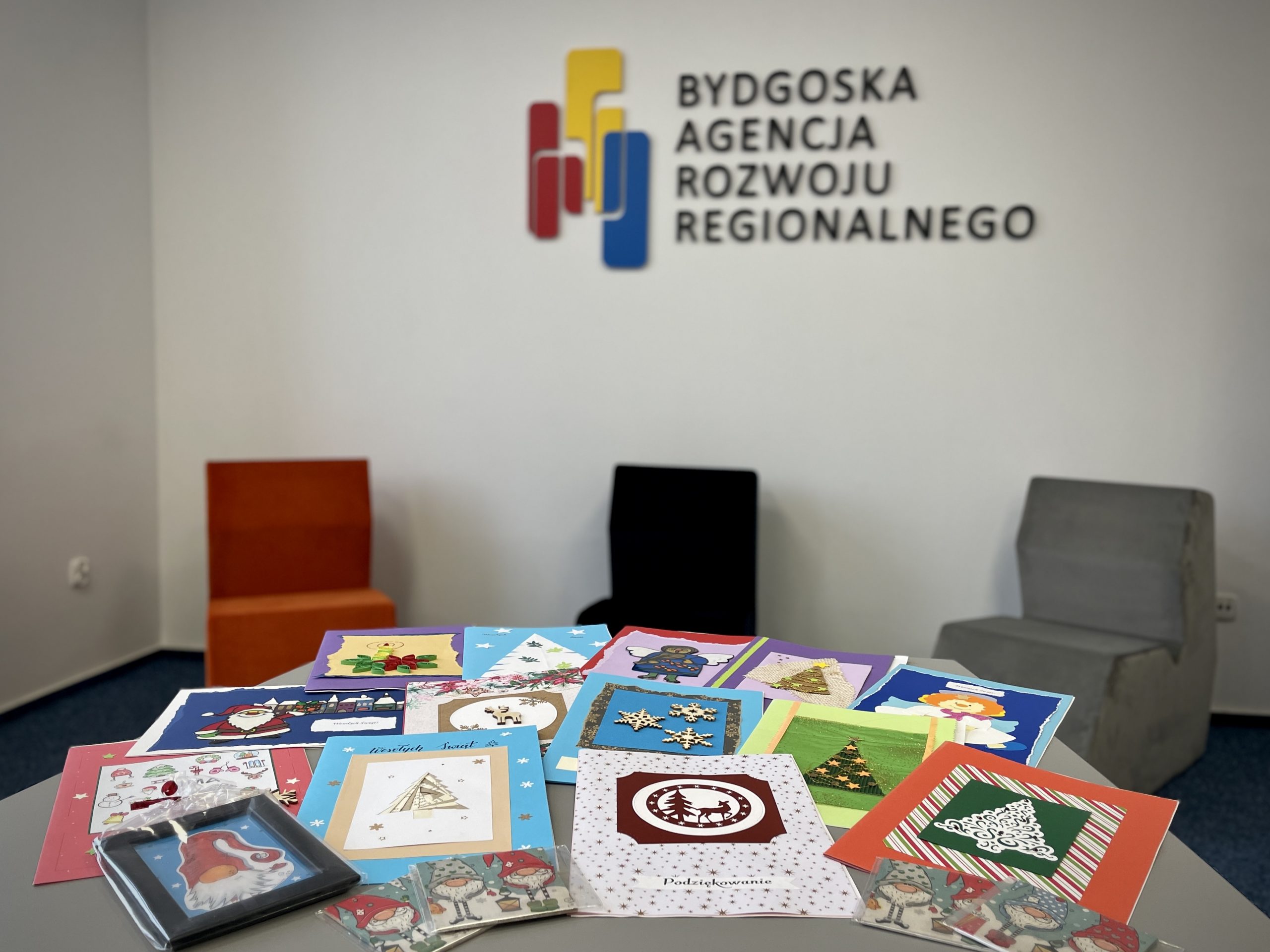 SU_2022_03 Kolorowe kartki świąteczne wykonane przez dzieci leżą na stole, w tle logo Bydgoskiej Agencji Rozwoju Regionalnego