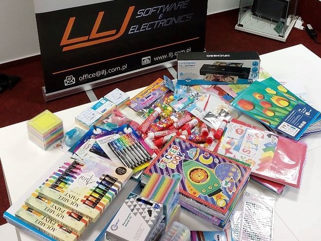 SU_2022_05_2 Upominki i materiały papiernicze leżą na stole, w tle logo firmy LLJ Softwar & Electronics