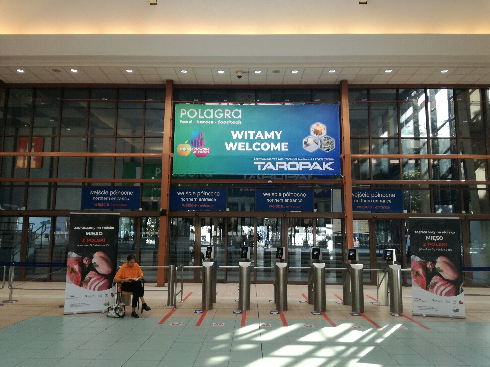Szklane dzrwi hali, wejście na targi, nad mini wisi billboard witamy