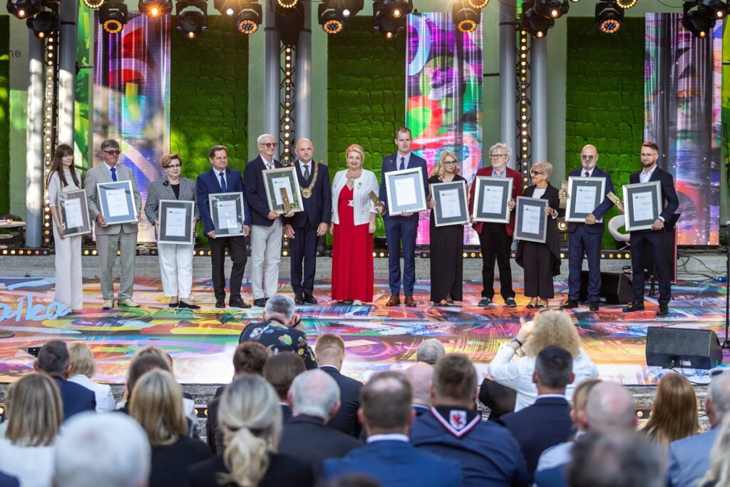 Laureaci Nagrody Marszałka w kategoriach gospodarka, fundusze unijne i innowacyjne metody stosowania w zakresie rozwoju promocji miast i obszarów wiejskich 10 Laureatów stojących na scenie trzymających wyróżnienia w postaci dyplomów oprawionych w ramki