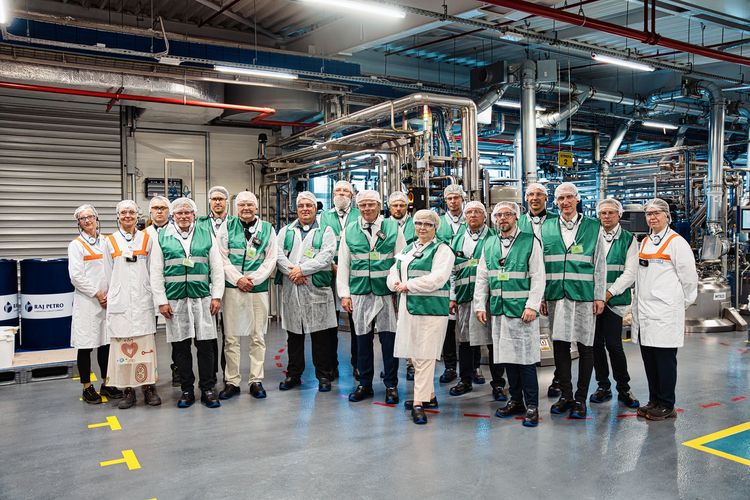 Uczestnicy otwarcia ubrani w fartuchy, kamizelki i czepki pozują do wspólnego zdjęcia wewnątrz magazynu.