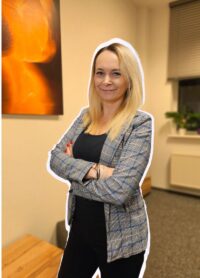 zdjęcie profilowe dr. Anita Kubanek, szczupła, długie blond włosy , stoi ze splecionymi rękoma w szarej marynarce i czarnych spodniach.